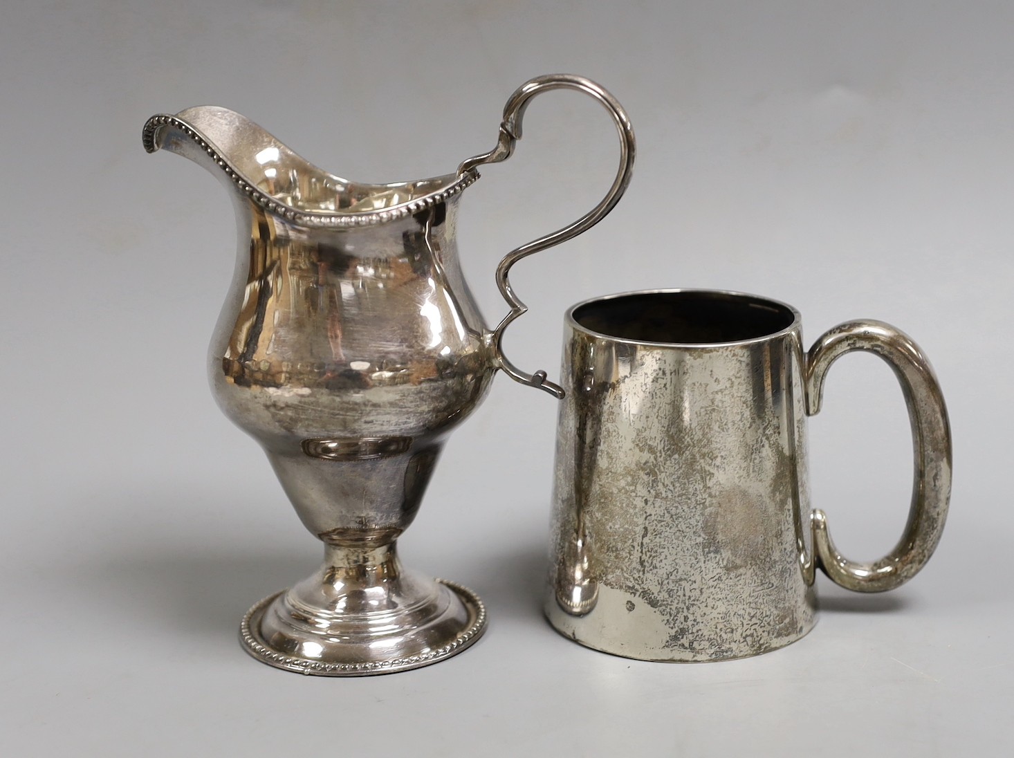 A George III silver inverted pear shaped cream jug, marks rubbed, 72mm and a later silver christening mug.